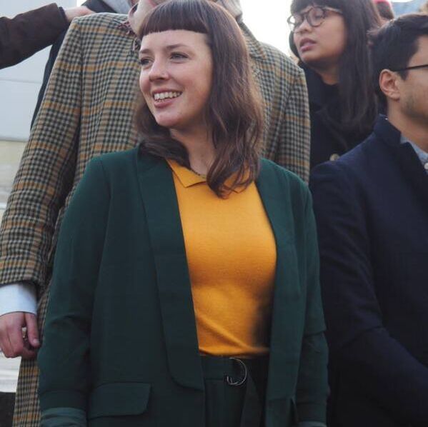 A picture of Lyndsay. Lyndsay's got a stark fringe and long brown hair. Lyndsay is also wearing a yellow top with a green cardigan on top in this image.