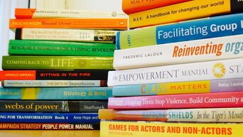 Two piles of colourful books next to each other. Some book titles are: 'Facilitating groups', 'Reinventing Organisations', 'Coming back to life', 'Webs of power'.